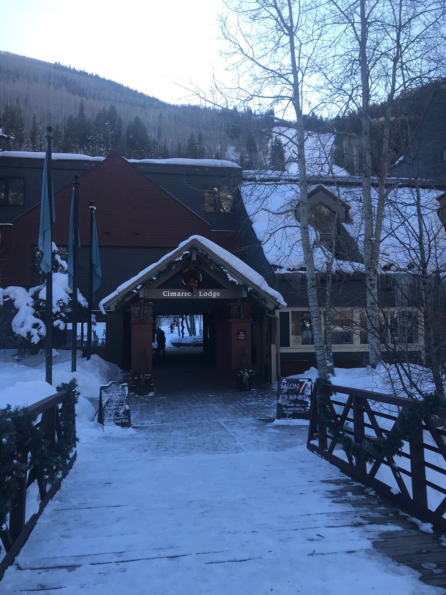 A lodge entrance with a snow-covered path leading to it, a sign for 'Cimarro Lodge', and a 'Salon' sign with a phone number.