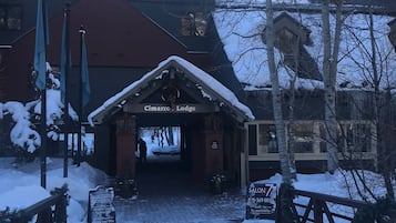 A lodge entrance with a snow-covered path leading to it, a sign for 'Cimarro Lodge', and a 'Salon' sign with a phone number.