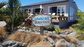 A beachfront house named Kawai Bay Beach House with a wooden deck and a sign. -  Comfort and relaxation at Kawau Bay Beach House.  (Snells Beach)
