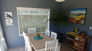 A dining area with a table, chairs, a potted plant, and a cabinet with items on top. -  Comfort and relaxation at Kawau Bay Beach House.  (Snells Beach)
