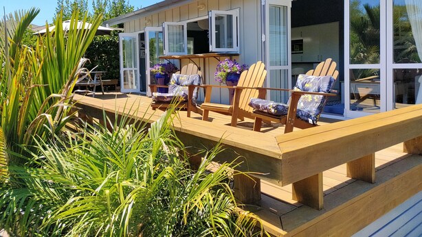 A wooden deck with outdoor seating, large windows, and potted plants. -  Comfort and relaxation at Kawau Bay Beach House.  (Snells Beach)