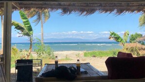 Vista a la playa desde un espacio techado con una mesa, sillas y botellas.