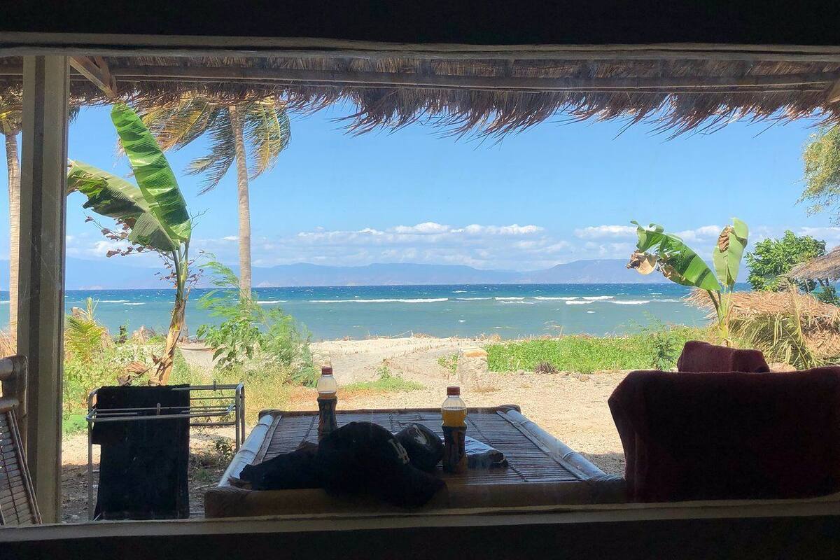 Uitzicht op het strand vanuit een beschut gedeelte met een tafel, stoelen en flessen.