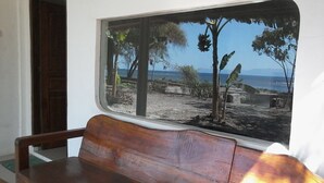 Un banco de madera en una habitación con un ventanal grande que da a una playa y un cielo despejado.