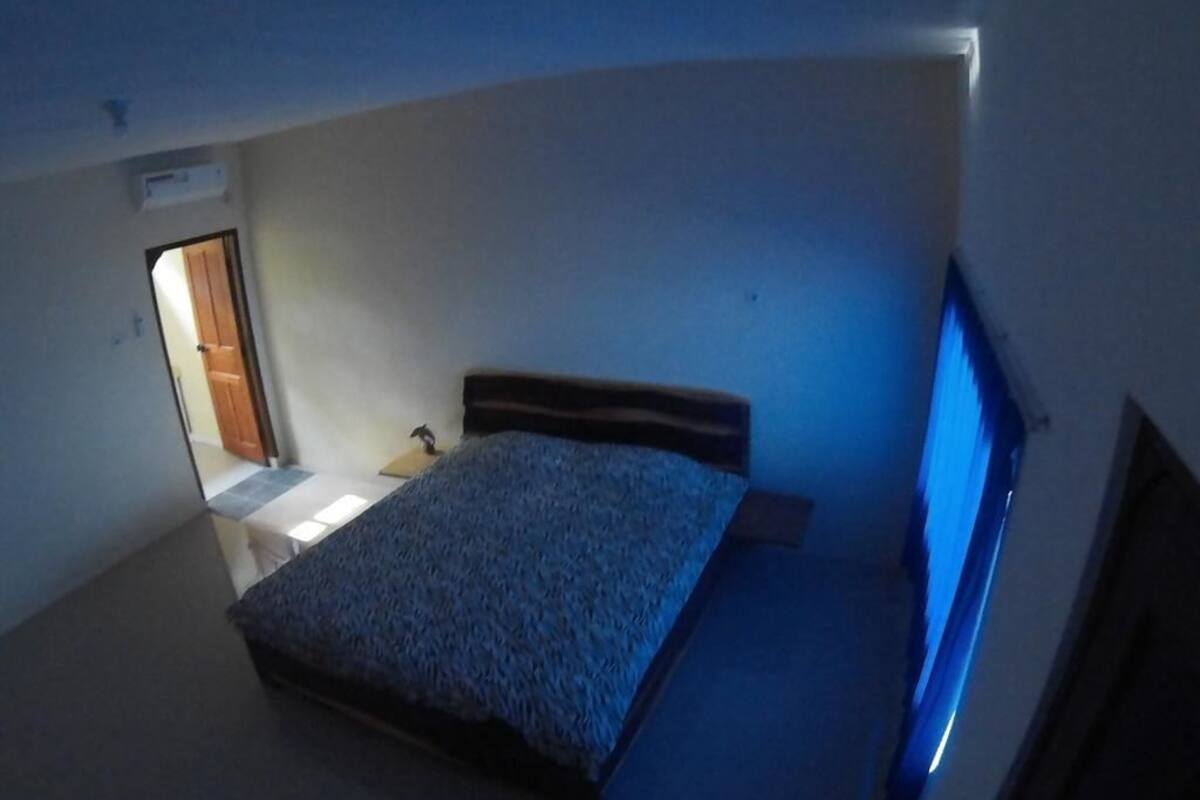 Een kleine, zwak verlichte kamer met een enkel bed, een tafeltje en een raam met uitzicht.