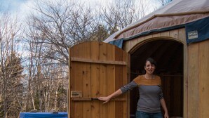 A wooden cabin with an open door, a hot tub, and a wooden deck.