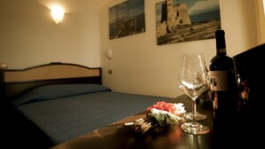 Een hotelkamer met een bed, een tafel met een fles wijn en een glas, en twee schilderijen aan de muur.