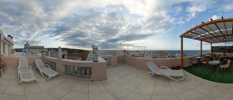 A rooftop terrace with lounge chairs, a covered seating area, and a view of the sea.
