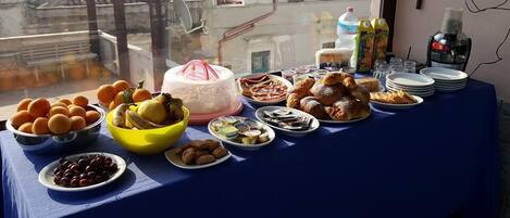 Una mesa con diferentes alimentos y un pastel, frente a una ventana que ofrece vistas de un edificio y una calle.