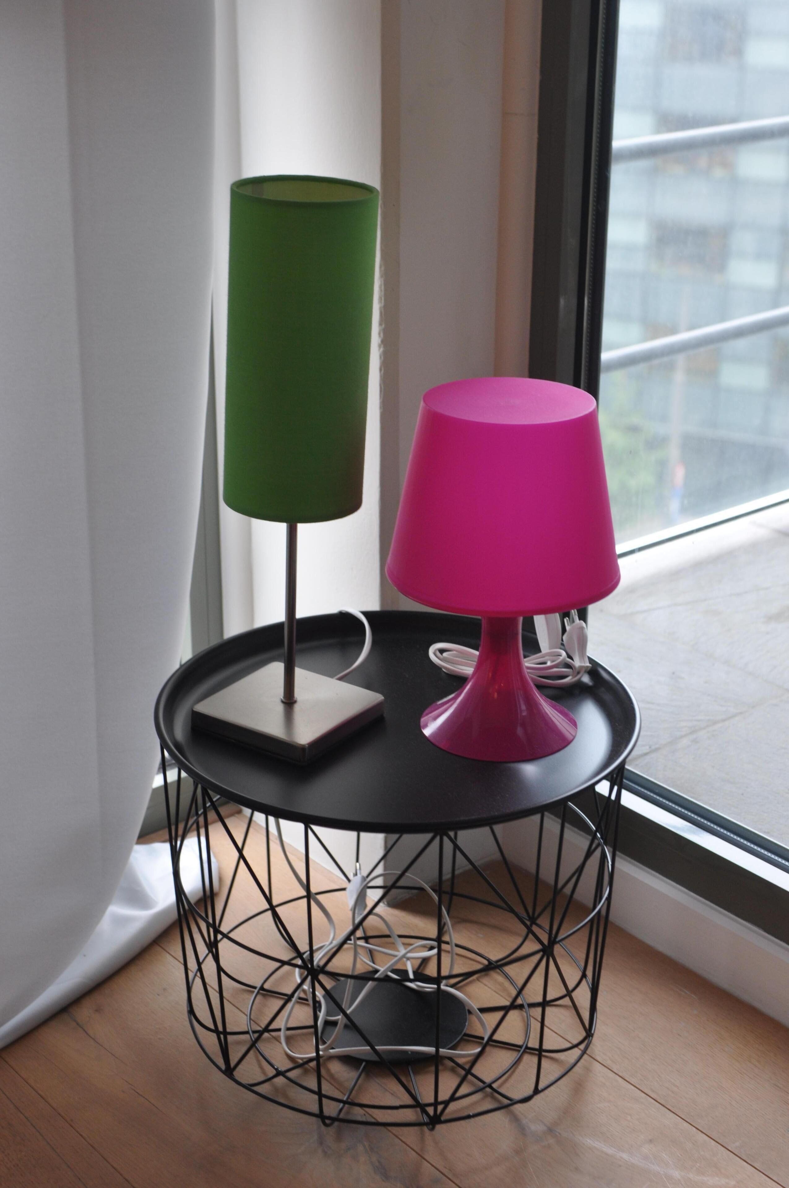A round table with a black wireframe base, two lamps (one green and one pink), and a power cord.