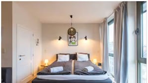 Una camera da letto con un letto, abat-jour, un quadro al muro e una finestra con tende.