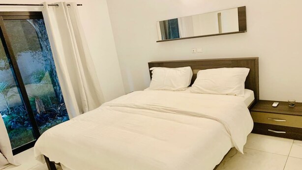 Une chambre à coucher comprenant un lit, une table de chevet, un miroir et une porte-fenêtre coulissante avec des rideaux.