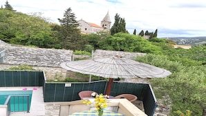 Eine Terrasss mit Pool, einem Tisch mit gelben Kissen und Blick auf ein historisches Gebäude im Hintergrund.