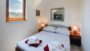 Ein Schlafzimmer mit einem Bett, zwei Nachttischen, einem Fenster und einem Spiegel.