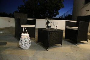 An outdoor patio with wicker furniture, a table with a bottle and glasses, and a white lantern. - B&B Pippi (Morciano di Leuca)