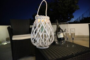 A wicker chair with a cushion, a white lantern, a bottle of champagne, and two glasses on a table. - B&B Pippi (Morciano di Leuca)