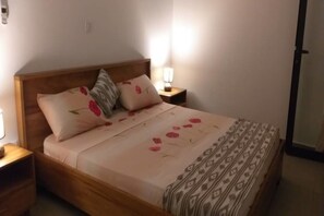 A neatly made bed with a floral bedspread and two pillows, a bedside table with a lamp, and a wooden headboard. - Résidence Anna 2 T3 (Abidjan)