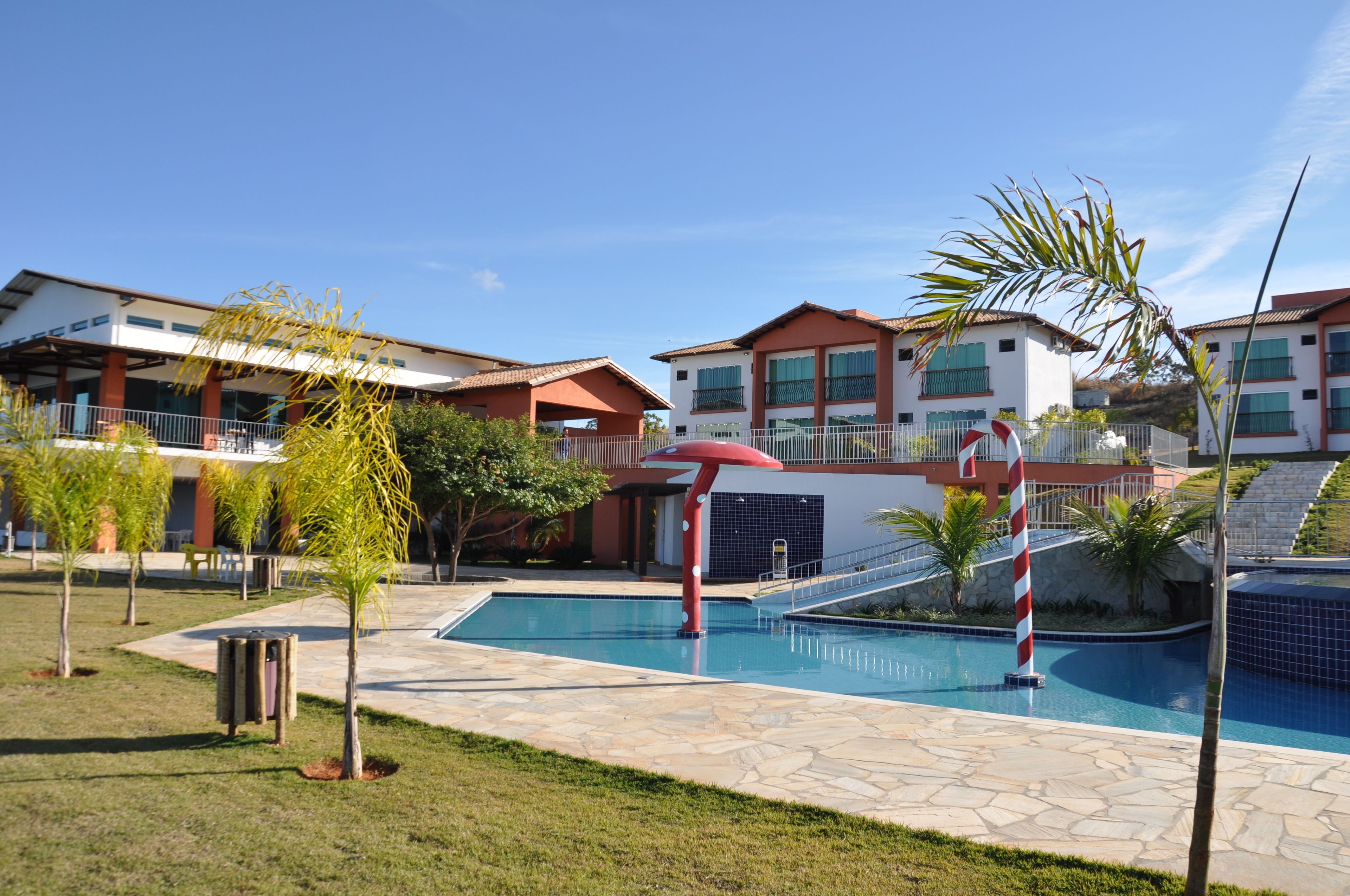A swimming pool area with a red and white striped pole, surrounded by buildings with balconies and a clear blue sky.