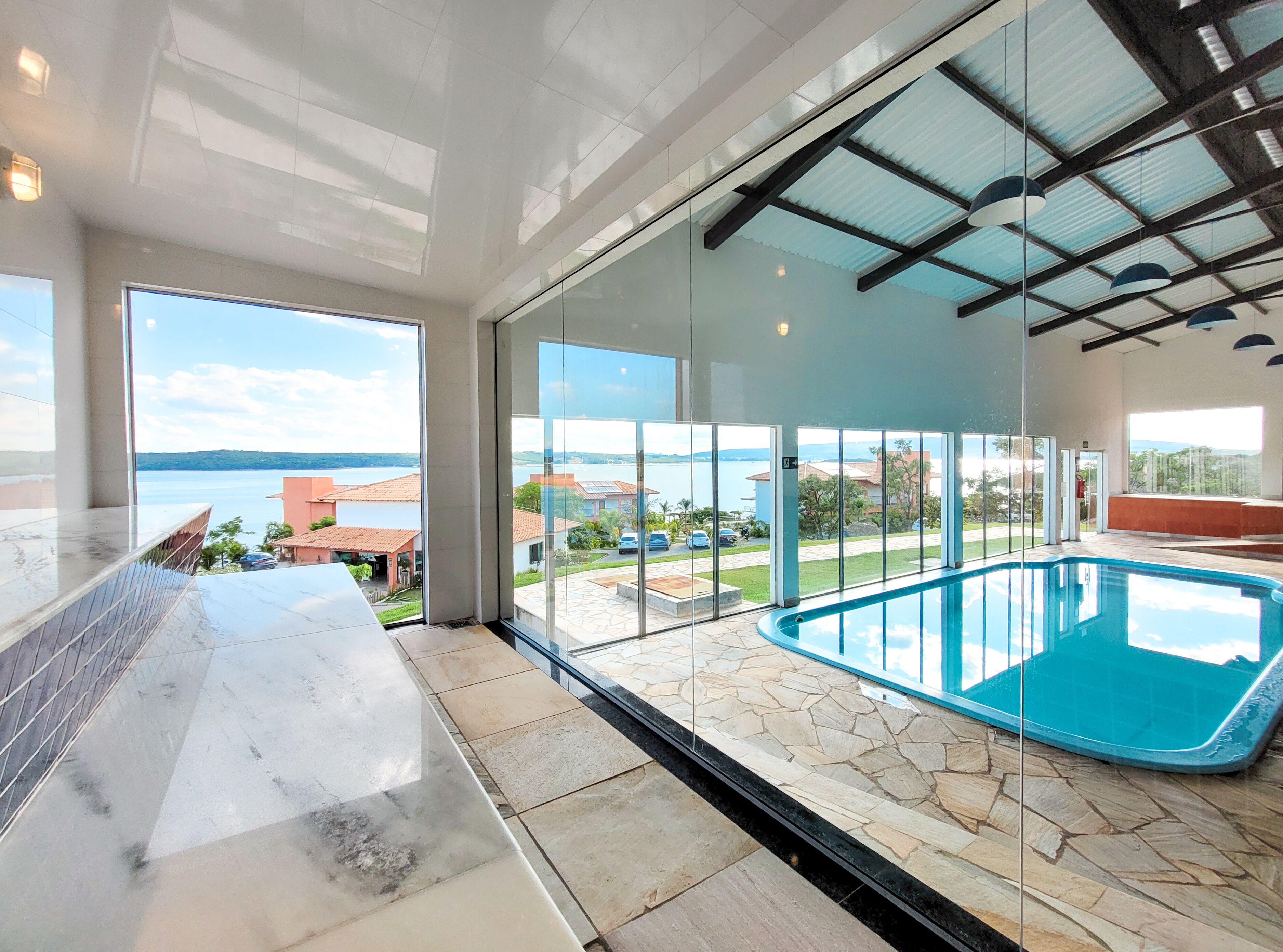 A modern interior with a glass-enclosed swimming pool, large windows offering views of the sea and surrounding buildings.
