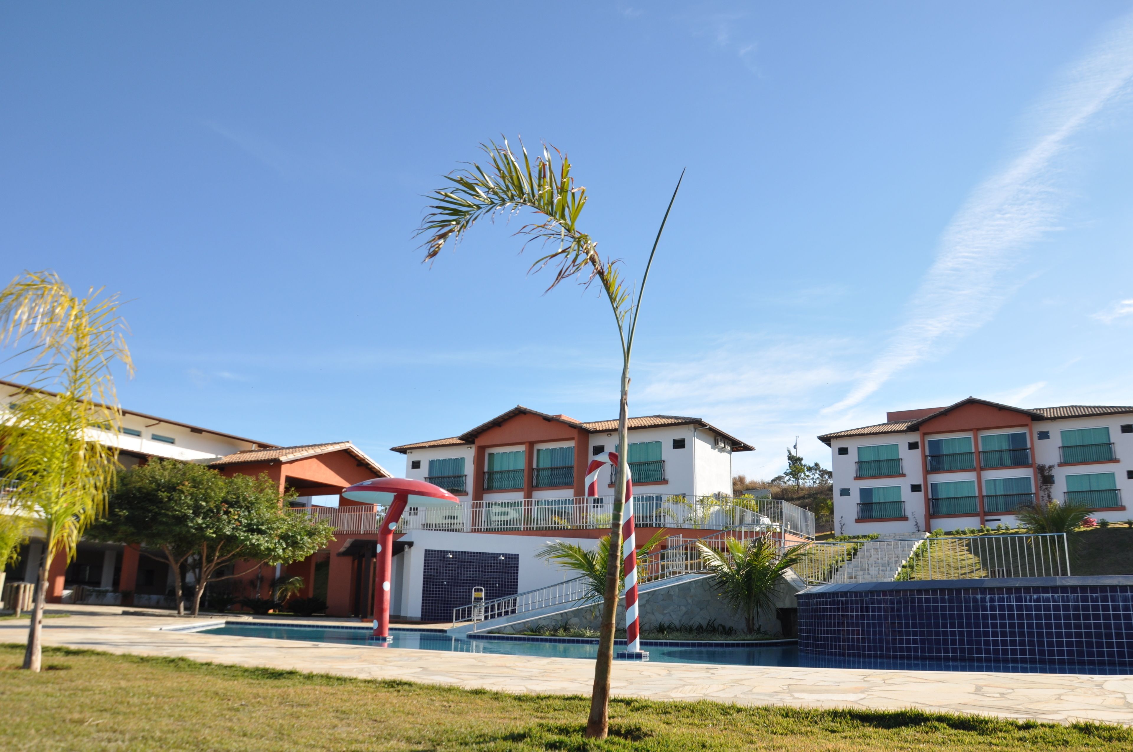 Un edificio moderno con piscina, una sombrilla roja y una palmera.