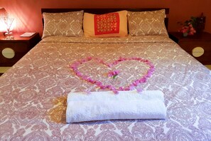 A neatly made bed with a heart-shaped flower arrangement and a rolled towel on a patterned bedspread. - Residence Anna T3 (Abidjan)