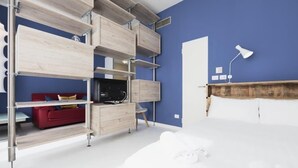 Un dormitorio con una cama, un sofá rojo y un televisor sobre una estantería de madera.