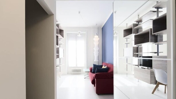 Una sala de estar moderna con un sofá rojo, una silla blanca y estanterías empotradas con un televisor de pantalla plana.