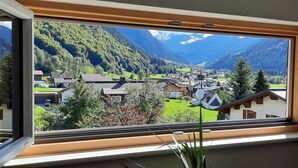 A modern room with a large window offering a view of a mountain village, a church, and lush greenery. - NEW, EXCLUSIVE, COZY apartment !!!! (St. Gallenkirch)