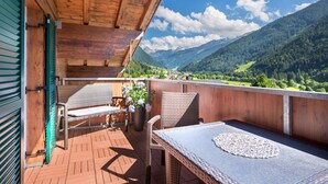 A wooden balcony with wicker furniture and a table, overlooking a mountainous landscape. - NEW, EXCLUSIVE, COZY apartment !!!! (St. Gallenkirch)