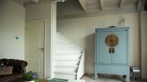A staircase leading to a landing, a blue cabinet with a circular door, a brown leather sofa, and a wooden table with a book and a potted plant.