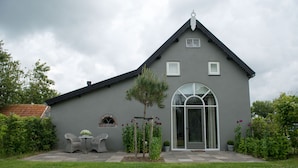 A gray house with a sloped roof, a large arched window, and a small porch with wicker chairs.
