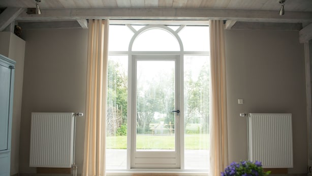 A room with a large glass door leading to a garden, a radiator on the wall, and a potted plant on the floor.