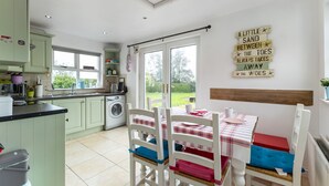 A bright kitchen with a washing machine, a dining area with a checkered tablecloth, and a sign on the wall. - Ballyginny Cottage (Castlewellan)