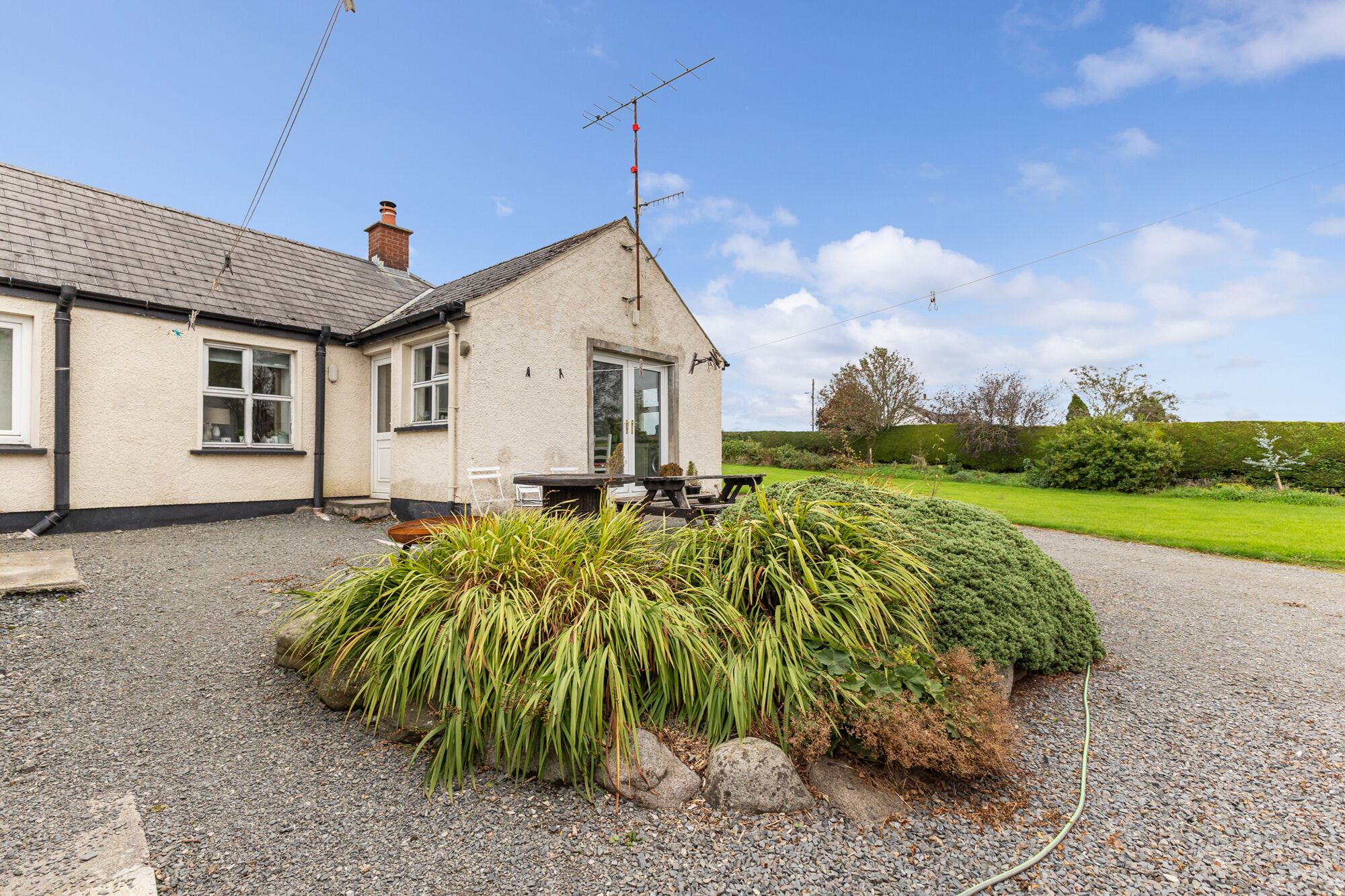A house with a gravel driveway, a patio with outdoor furniture, and a well-maintained garden.