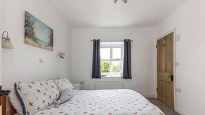 A bedroom with a bed, a window with curtains, a radiator, and a door. - Ballyginny Cottage (Castlewellan)
