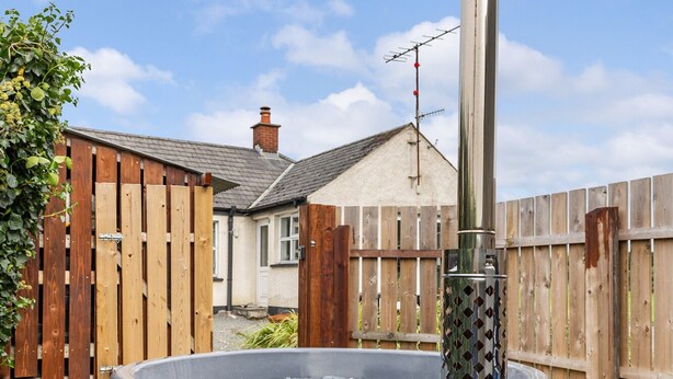 A wood-burning stove with a chimney, surrounded by a wooden fence and a house in the background. - Ballyginny Cottage (Castlewellan)
