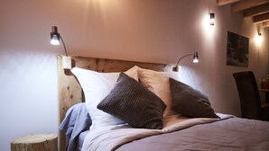 A neatly made bed with a wooden headboard, two bedside lamps, and a small round stool. - La Foyère (Aime-la-Plagne)