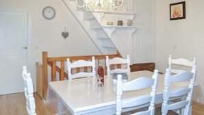 A dining area with a white table, white chairs, a wooden chair, a clock, a heart-shaped decoration, and a staircase.