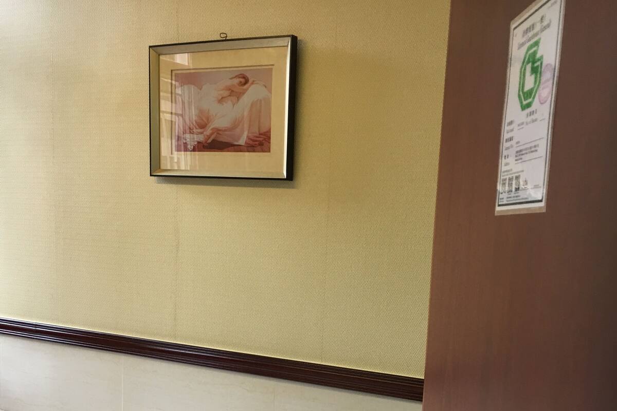 A small, single-bed room with a wooden headboard, a framed picture on the wall, and a door with a number sign.