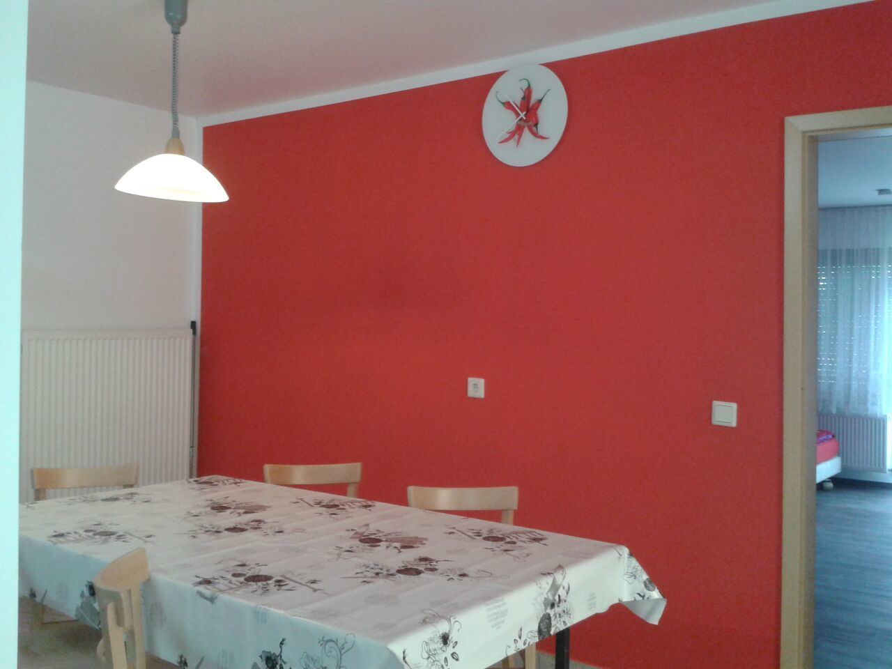A dining area with a table set for four, red walls, and a ceiling light.