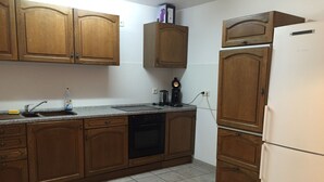 Een keuken met houten kastjes, een vaatwasser, een koelkast en een aanrecht met een spoelbak en een koffiezetapparaat.