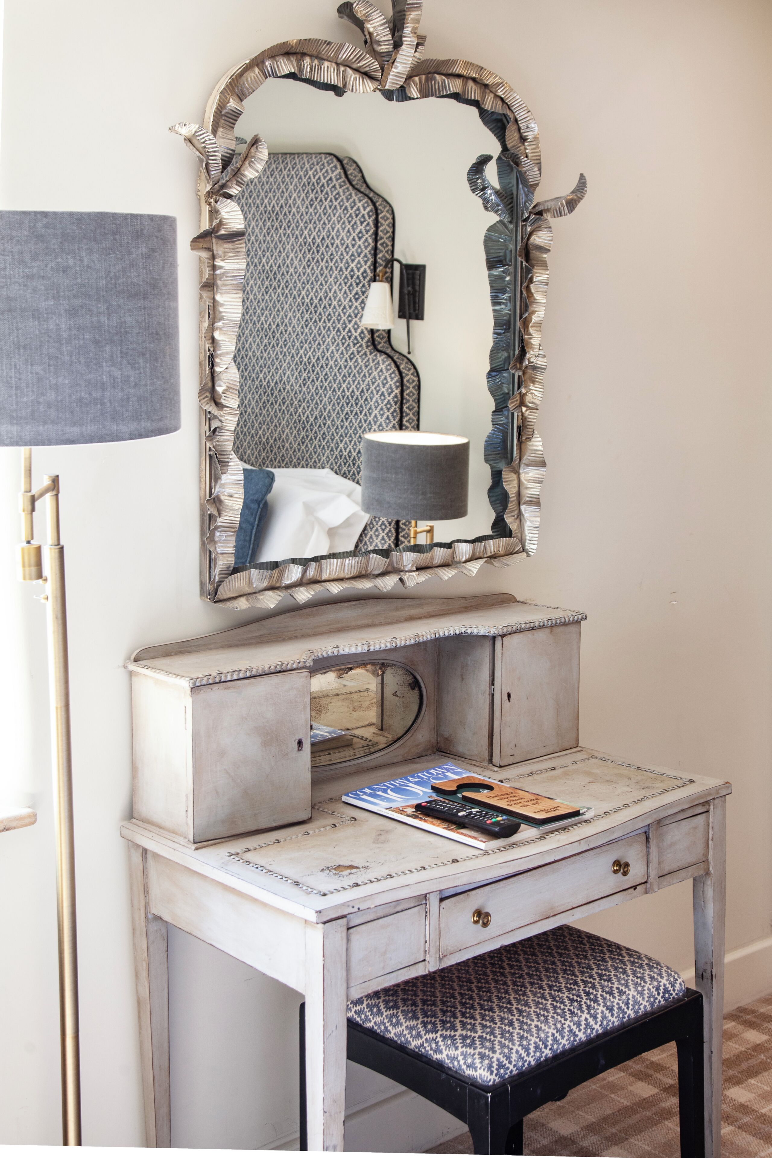A vintage vanity with a mirror, a lamp, and a small table with a magazine.