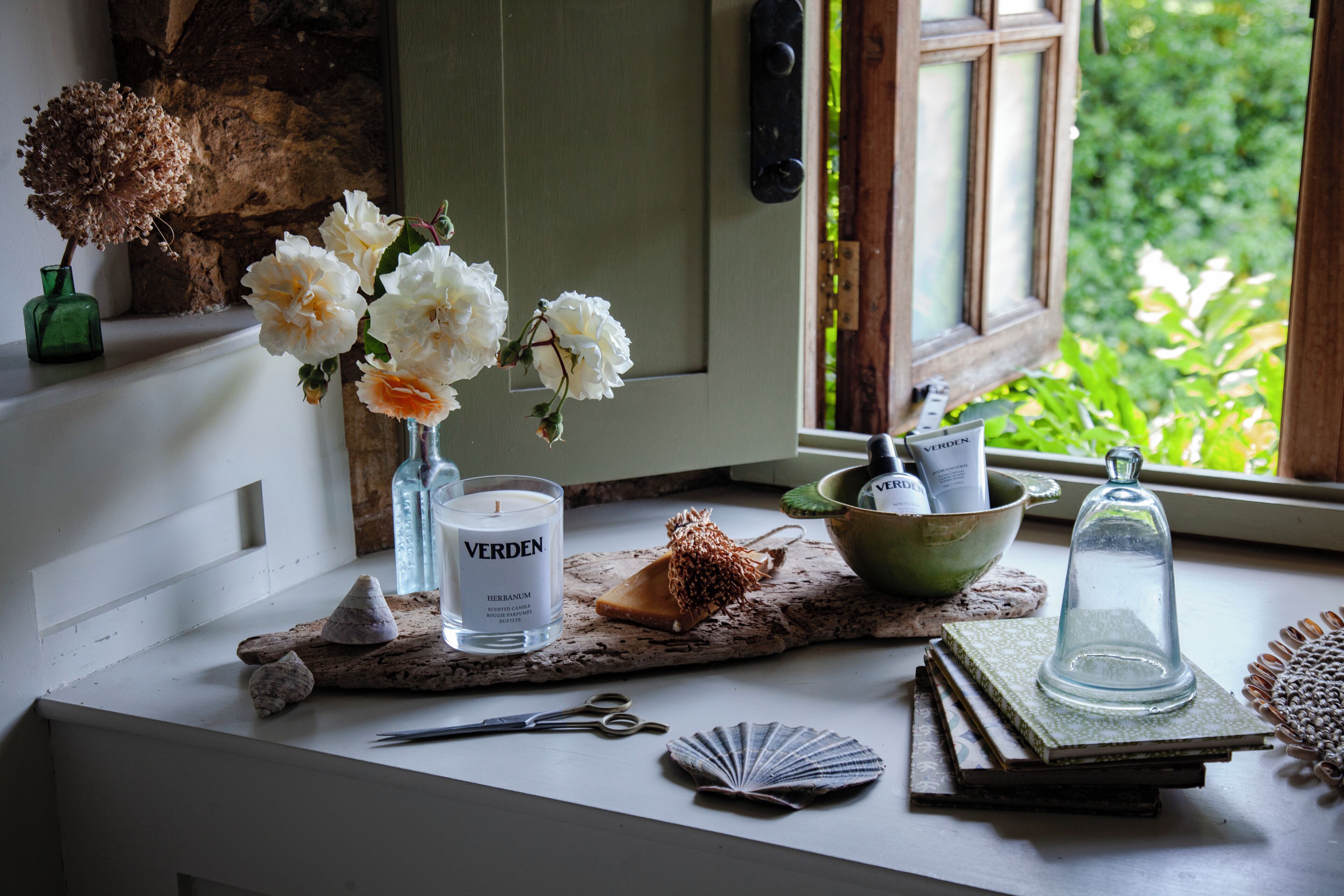 A table with a candle, a vase with flowers, a bowl, and a book.
