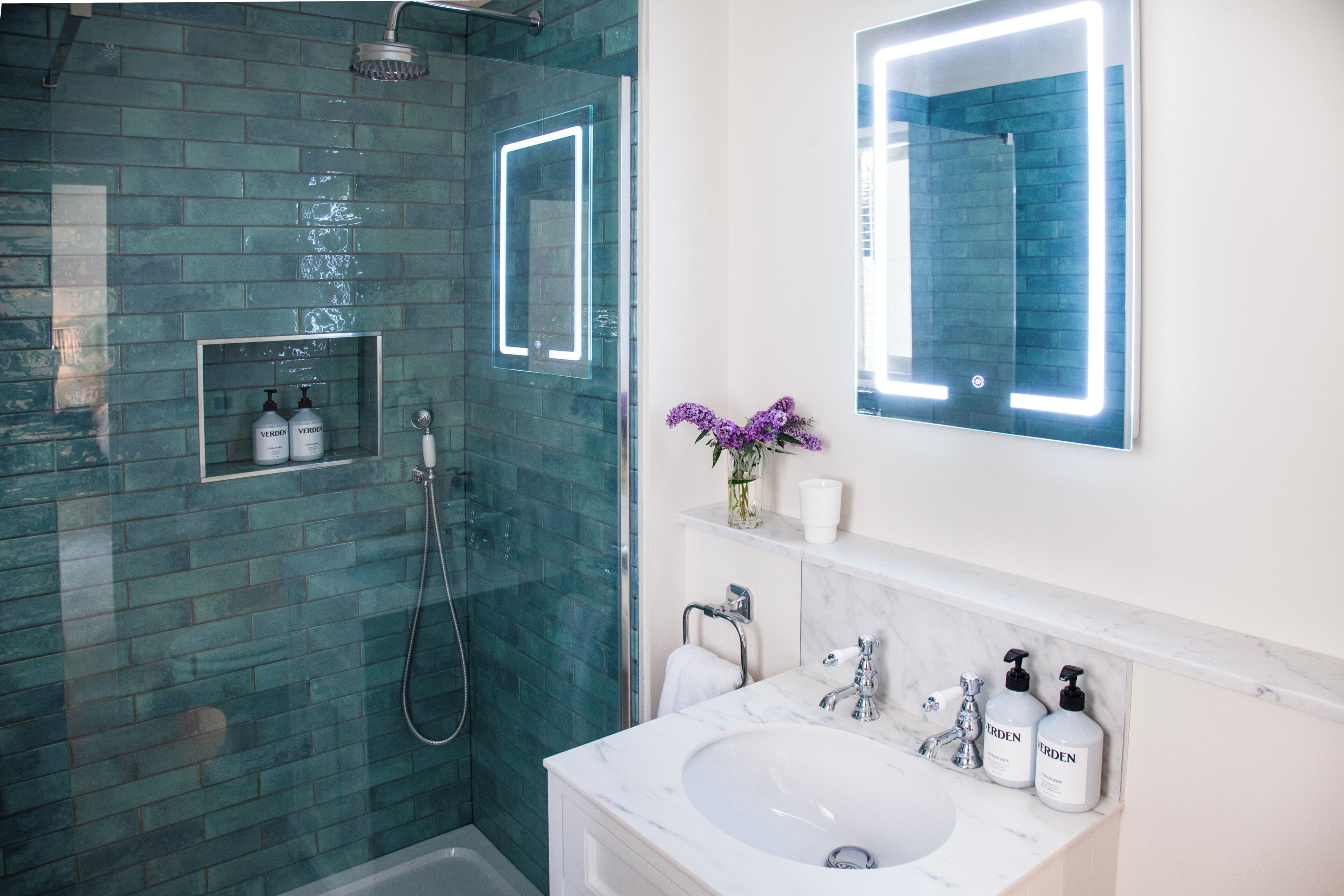 A modern bathroom with a glass-enclosed shower, a white sink, and a mirror with a lighted frame.