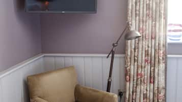Una habitación con un televisor de pantalla plana montado en la pared, un sillón color beige, una lámpara de pie y una alfombra a cuadros.
