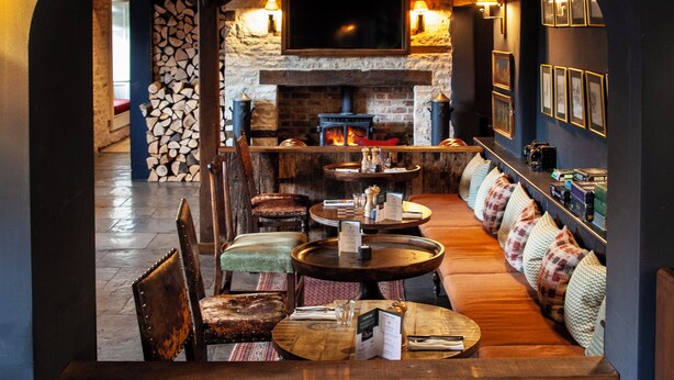 A cozy restaurant with a fireplace, wooden furniture, and a stone wall. - The Harcourt Arms (Witney)