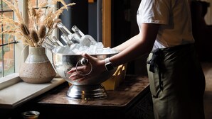 A person arranging glasses on a bar counter near a window with a brick wall view. - The Harcourt Arms (Witney)