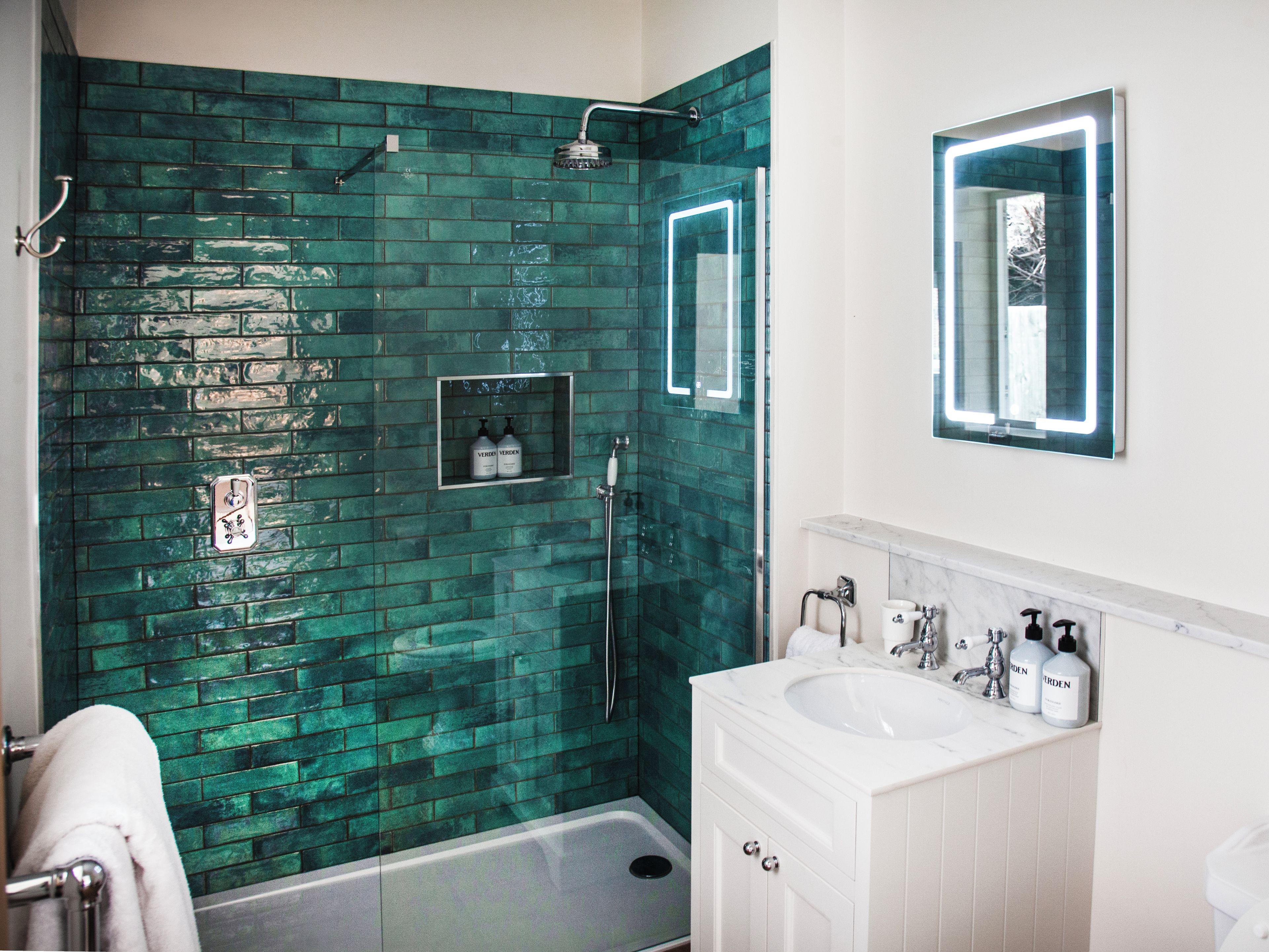 Un baño con pared de ducha de azulejos verdes, un lavabo blanco con encimera de mármol y un espejo sobre el lavabo.