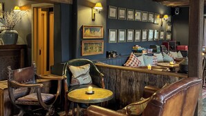 A cozy bar area with wooden beams, leather chairs, a small round table with a candle, and framed pictures on the wall. - The Harcourt Arms (Witney)