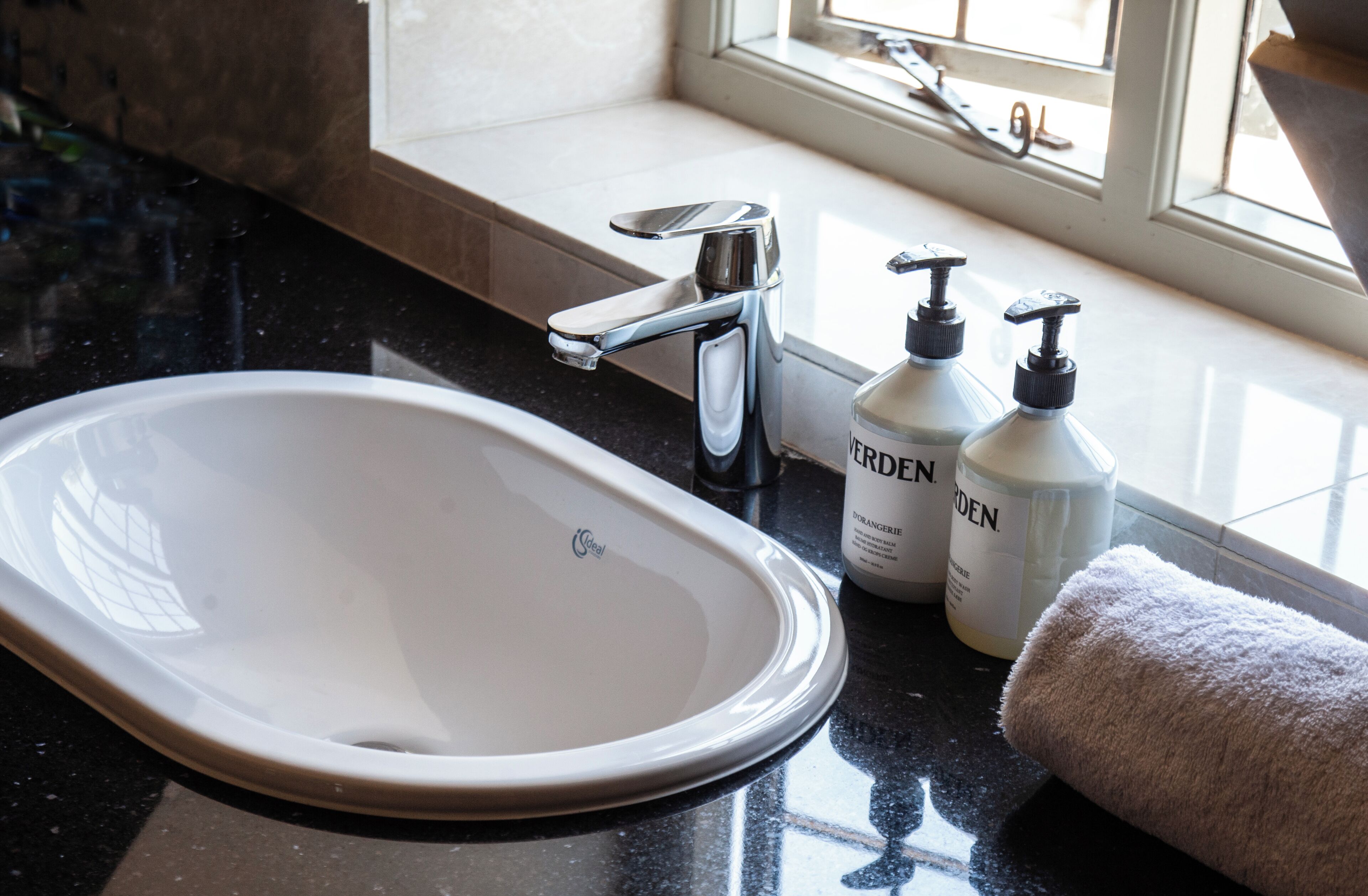 A bathroom with a white sink, a faucet, two bottles of hand sanitizer, and a towel.